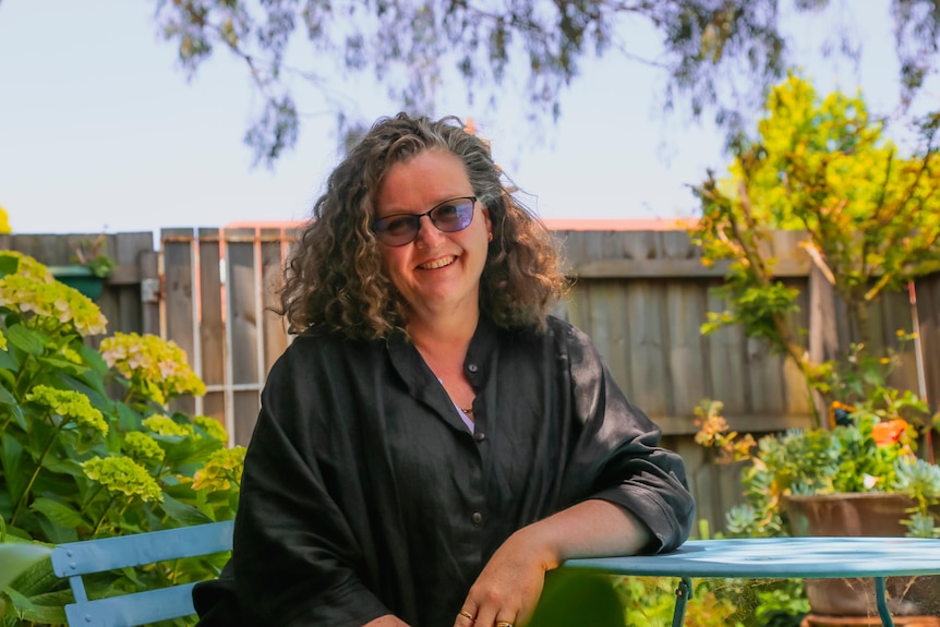 A woman sitting at a small outdoor table in what looks like a suburban backyard