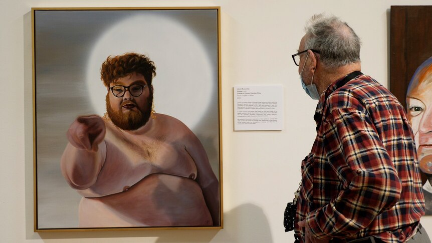 An elderly farmer wearing flannelette shirt looks at a portrait of a shirtless Connor Ovenden-Shaw