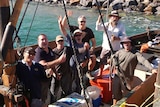 Seven men stand in a boat on the ocean.