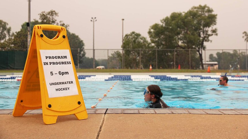 A photo of people swimming across the swimming pool, with an underwater hockey sign visible in front.
