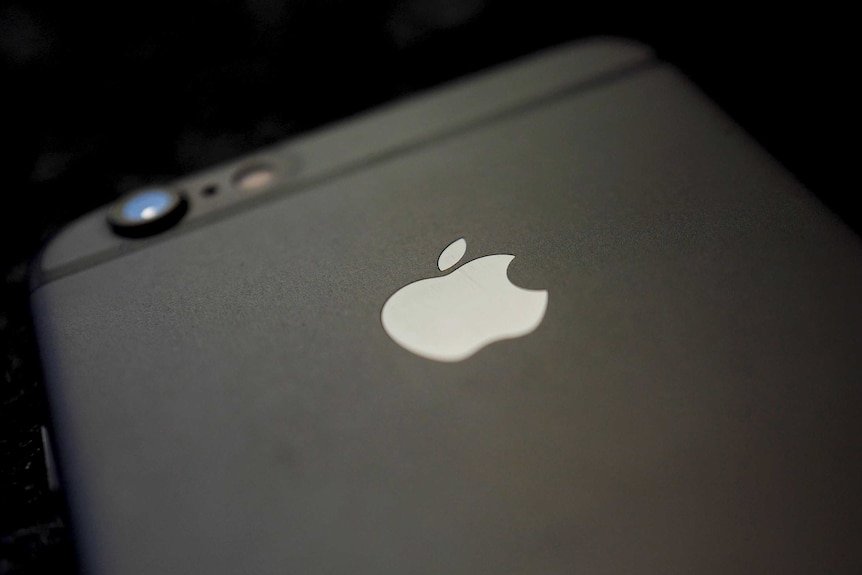 The back side of an iPhone 6 sits on a table in dark lighting.