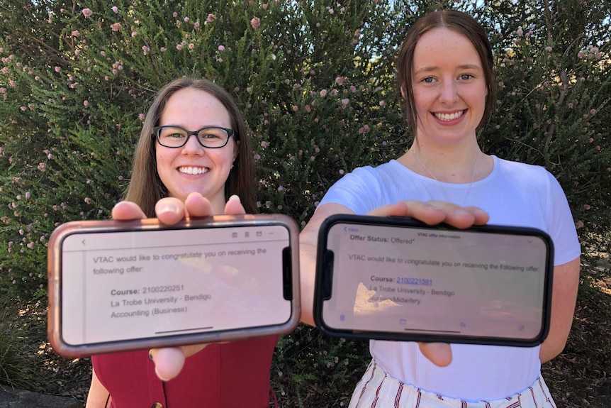 Two young women hold their phones out in front of them that show their university offers