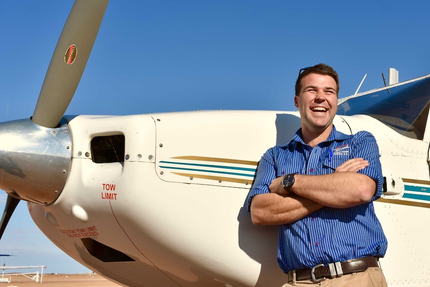 A man in a blue shirt leans on a plane.  He is smiling