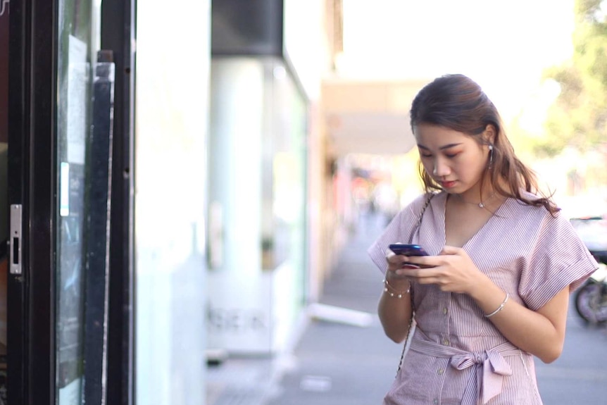 Angela Zhang is looking down at her phone as she walks into a shop.