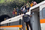 A group of people stand on top of a train that is halfway inside a tunnel