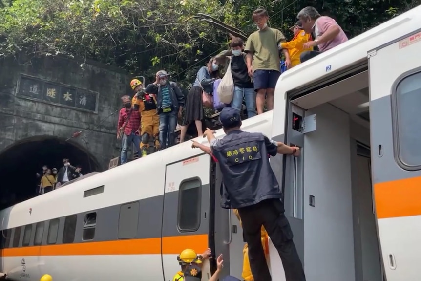 A group of people stand on top of a train that is halfway inside a tunnel