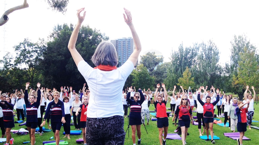 Yoga instructor and participants raise their arms