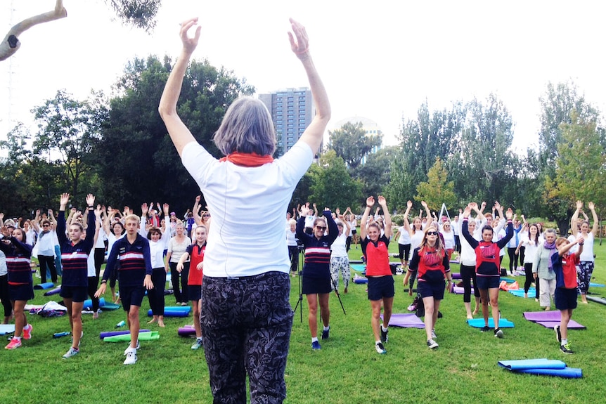 Yoga instructor and participants raise their arms