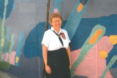 Woman standing in front of a mural of small tiles.