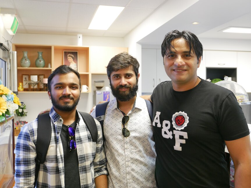 Three men pose for a photo in a bright retail store.