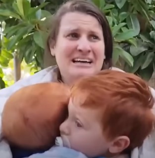A woman, with a panicked expression on her face, holds two children.