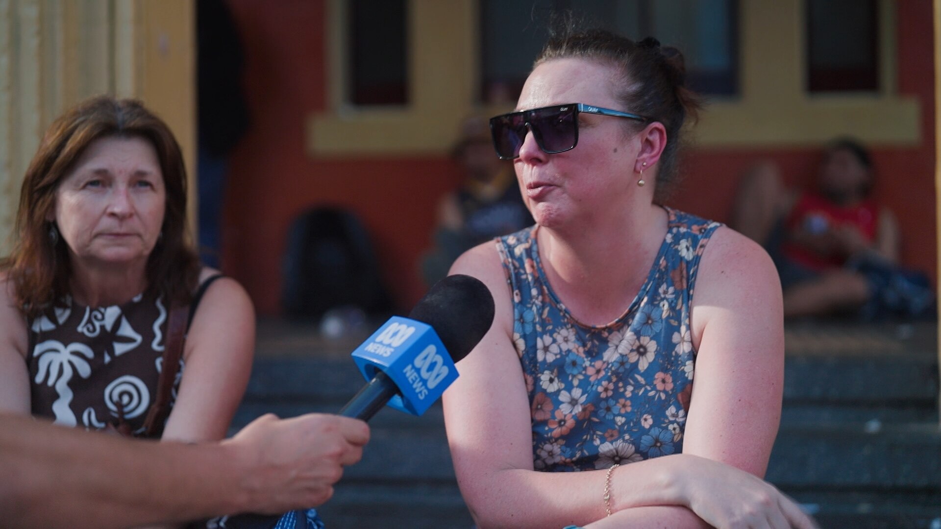 Una mujer con gafas de sol oscuras y una camiseta colorida espera ser transportada a casa.