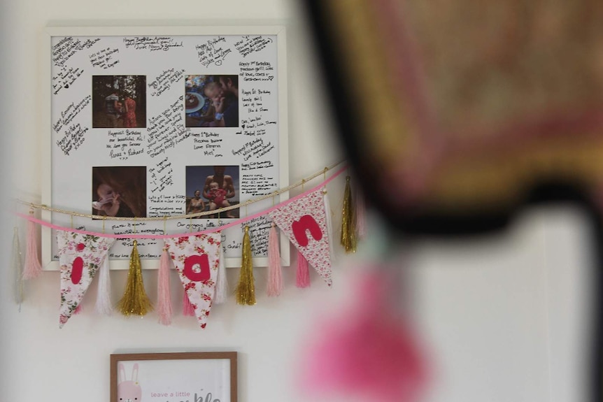 A photo, partly obscured by a hanging ornament, of a photo frame in Aviana's bedroom filled with photos and signatures.
