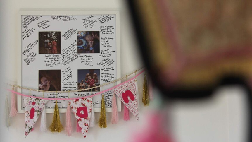 A photo, partly obscured by a hanging ornament, of a photo frame in Aviana's bedroom filled with photos and signatures.