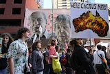 Protesters march along a street with one carrying a banner stating 'We're cactus mate' against an image of Australia burning