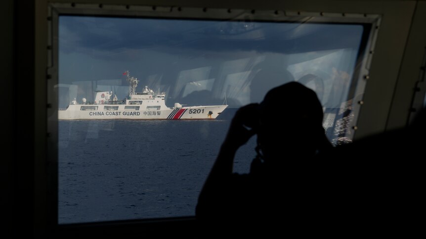 一名男子用望远镜眺望远处的中国海警船