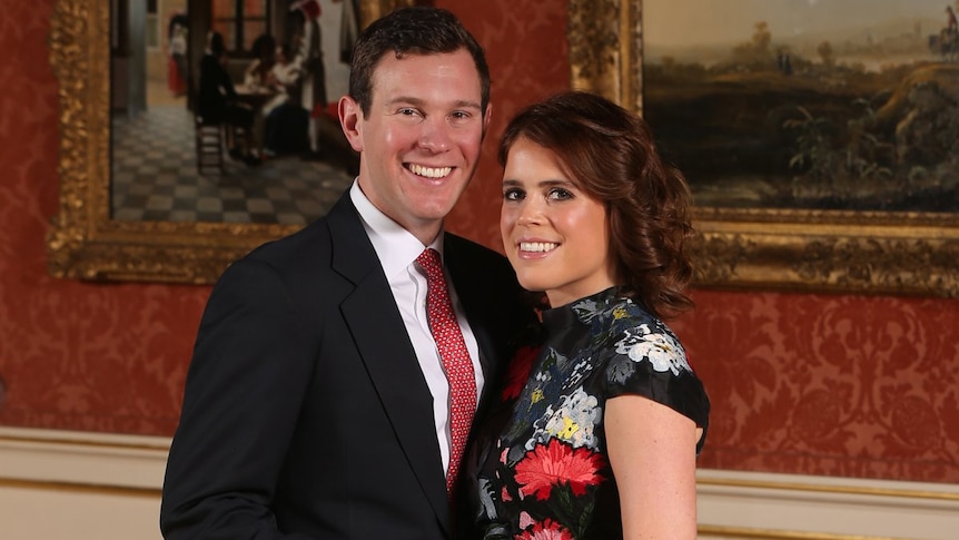 Jack Brooksbank holding Princess Eugenie close and holding her hand to show an engagement ring standing in front of paintings