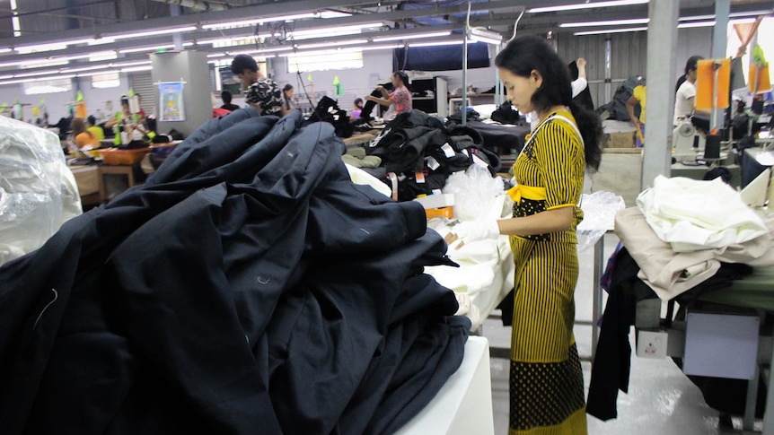 A woman in a yellow top and skirt stands next to a big pile of black fabric.