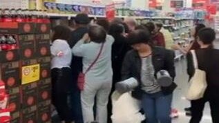 A crowd of people grouped at a small portion of a shopping centre aisle, grabbing baby formula tins.