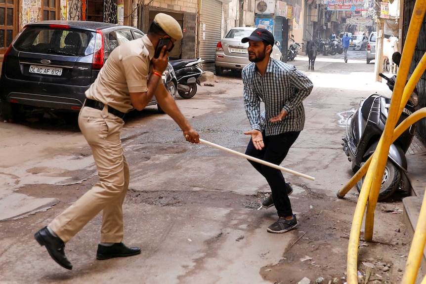 A cop talking on the phone whacks a man with a cane while he gestures at him