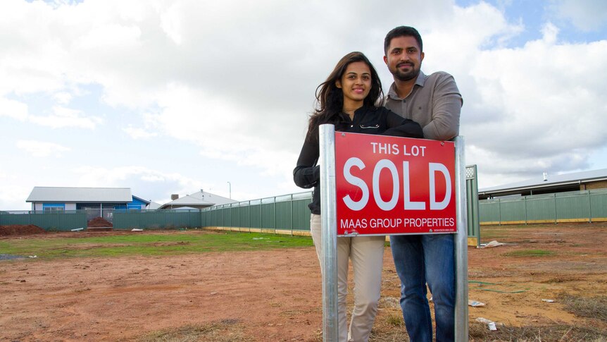A man and a woman standing next to a sold sign