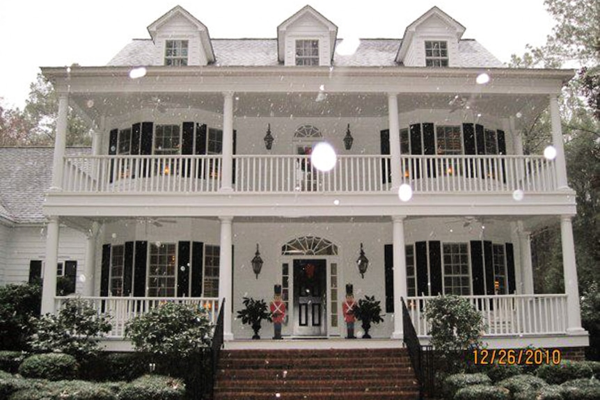 A white house with decorative railings and big bay windows decorated with christmas ornaments.