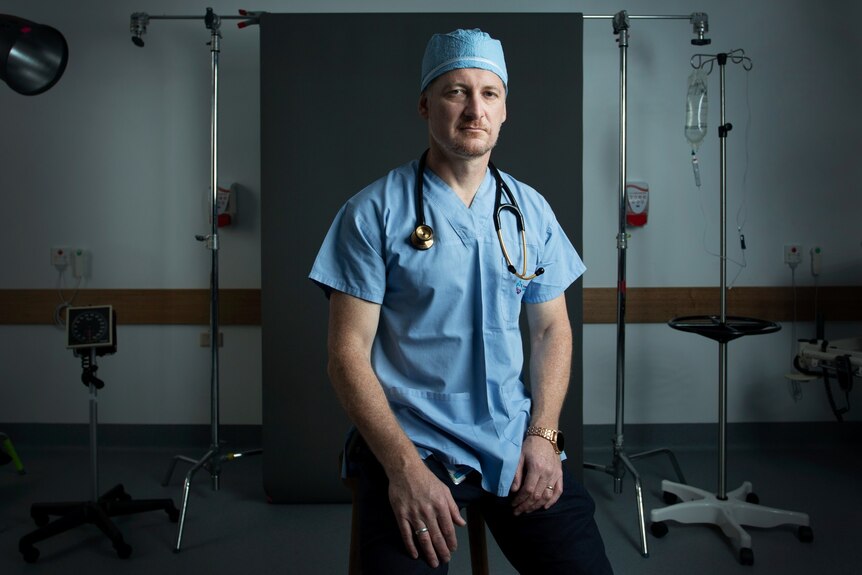 A middle-aged white man in blue scrubs with a stethoscope around his neck