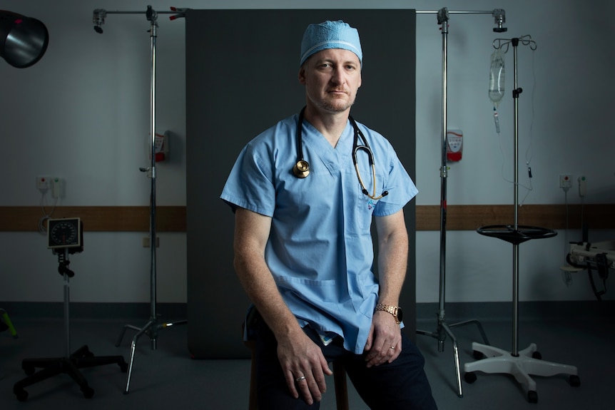 A middle-aged white man in blue scrubs with a stethoscope around his neck