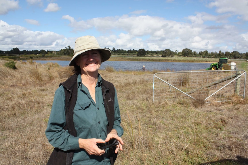 Female farmer stands in paddock with tractor in background.