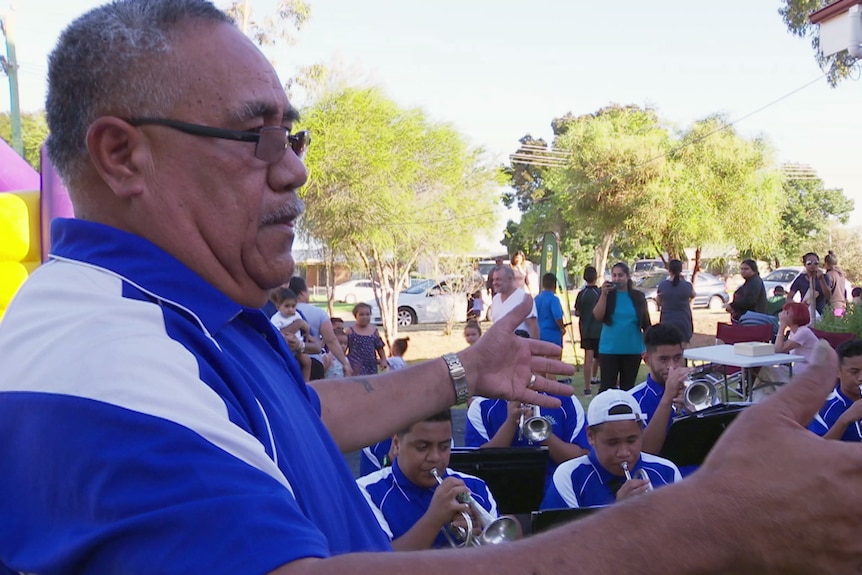 A Tongan man conducts a student brass band.