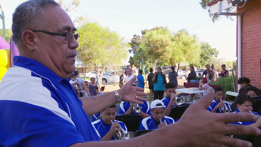 A Tongan man conducts a student brass band.