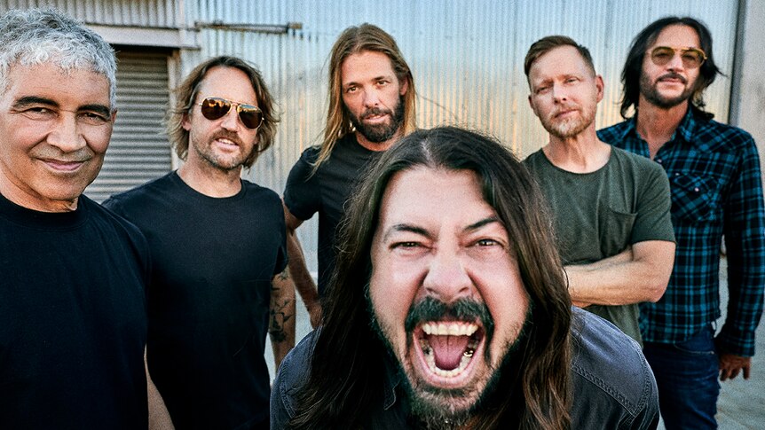 Six members of Foo Fighters stand in front of a corrugated iron shed
