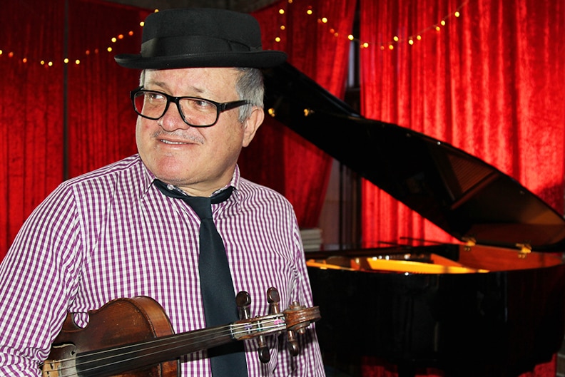 A profile shot of George Washingmachine standing, violin in hand, on the dancefloor of the Unity hall Hotel performance space.