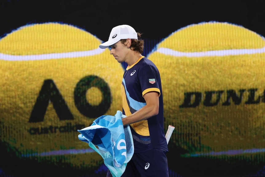 Alex de Minaur carries his towel as he walks in front of a projection of two tennis balls at the Australian Open.