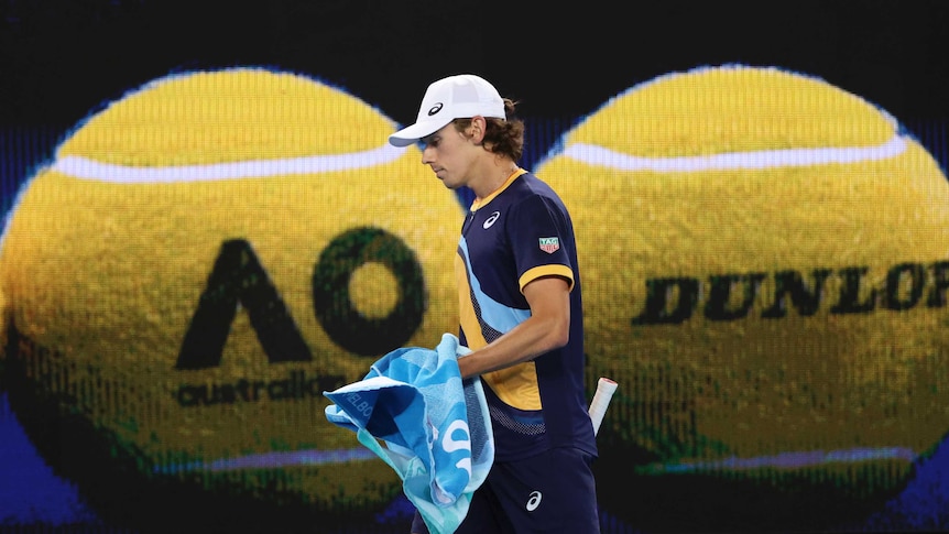 Alex de Minaur carries his towel as he walks in front of a projection of two tennis balls at the Australian Open.