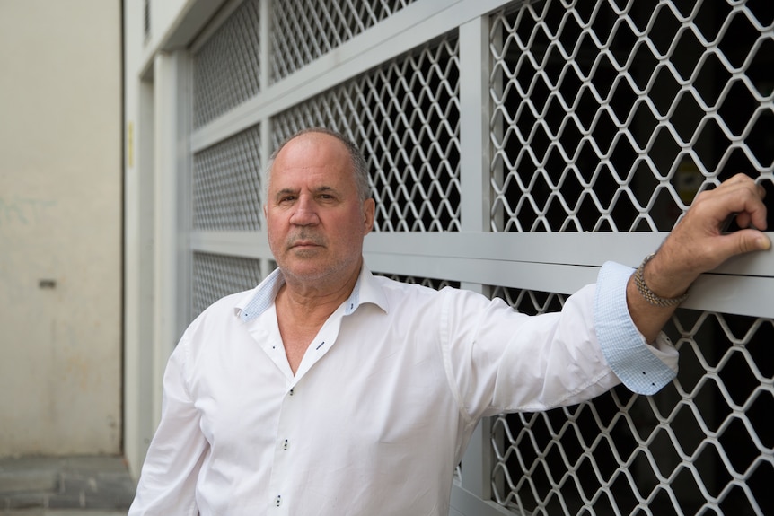 A man named standing in white button up shirt next to a fence in a street.