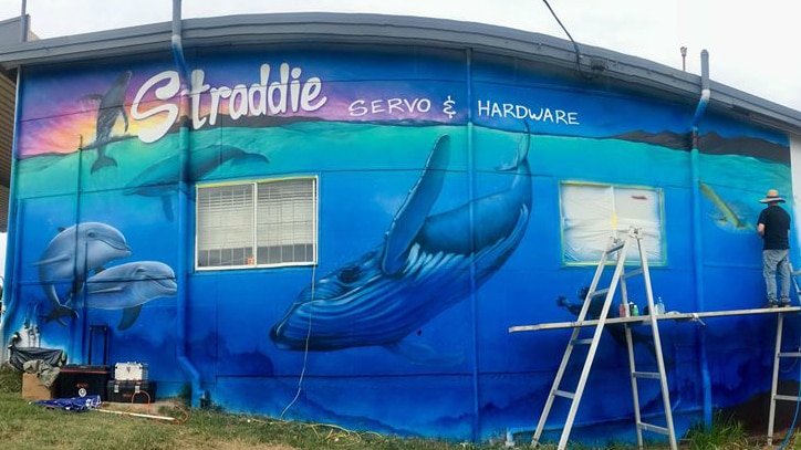 Man standing on ladders painting a large mural