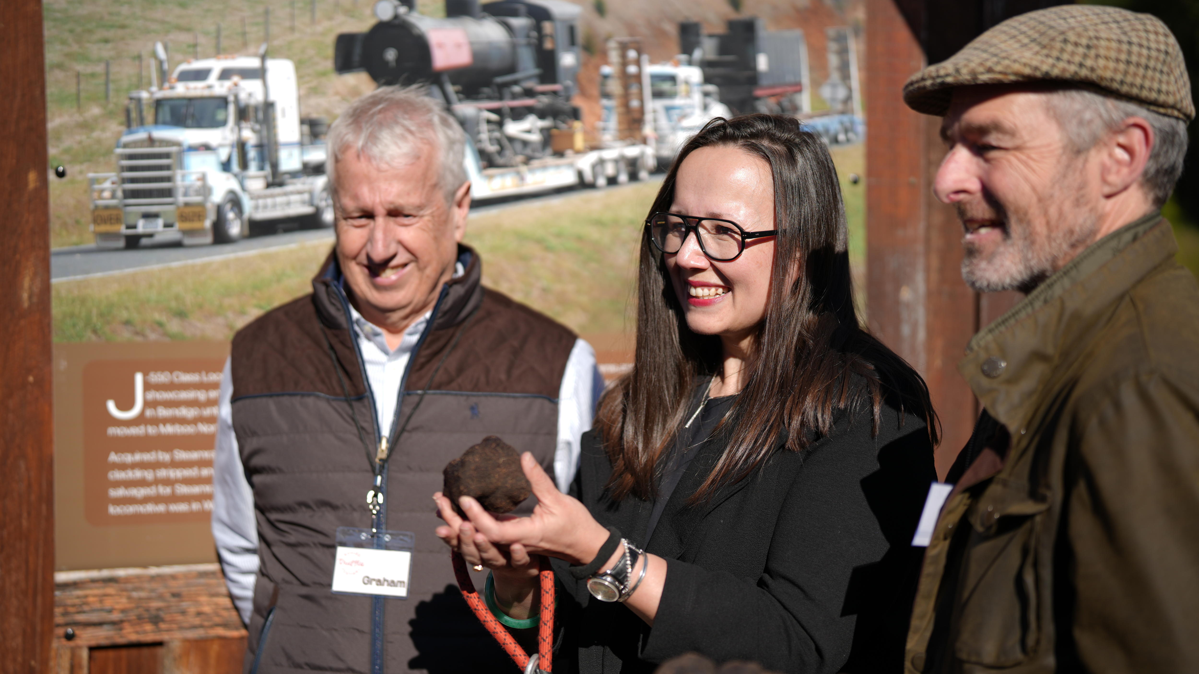 Image of two men and a woman, holding black truffles in their hands. 