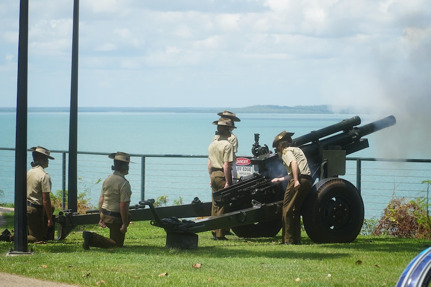 Members of the armed forced light the cannon, the ocean in the background.