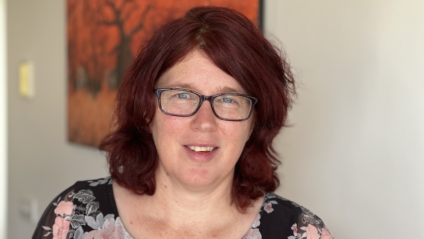 A woman with an auburn bob and glasses smiles.