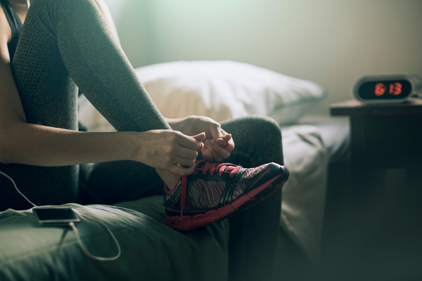 Woman sitting on bed tying her shoe laces