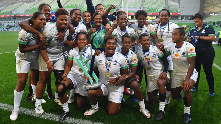 Fijiana Drua players celebrate winning the Super W final with the championship trophy.