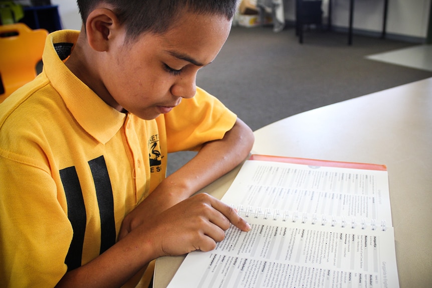 Tjabadungah Yanner looking over the dictionary, dressed in his yellow school uniform.