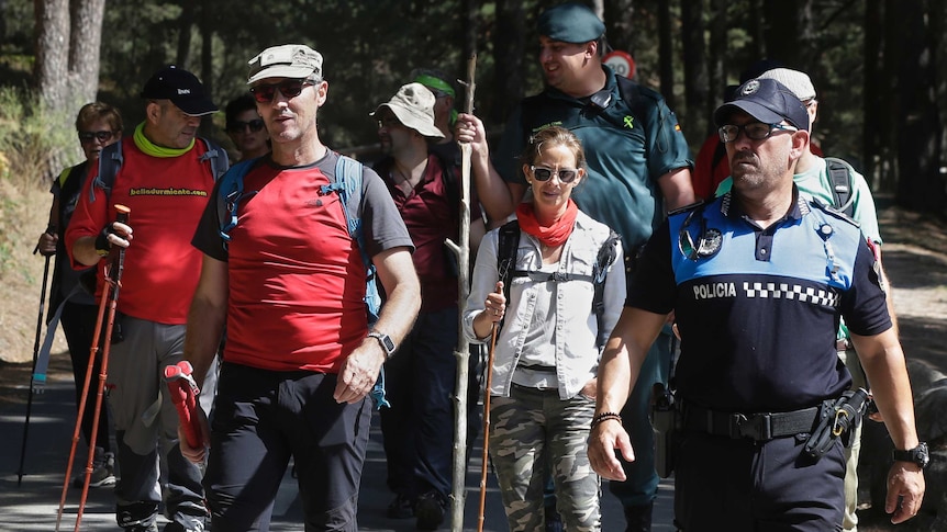 A group of men and women walk with sticks in their hands behind a police officer.