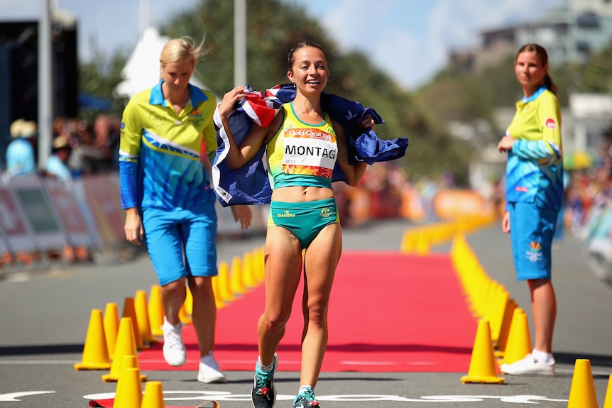 A woman wearing yellow and green walking with a blue and red flag over her shoulders