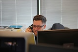 Man on the phone in an office in front of two desktop computer screens