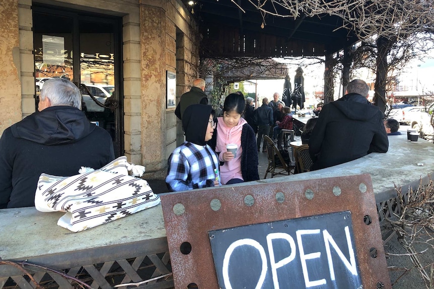 People sit outside on a deck of a restaurant on a sunny, blue sky day.