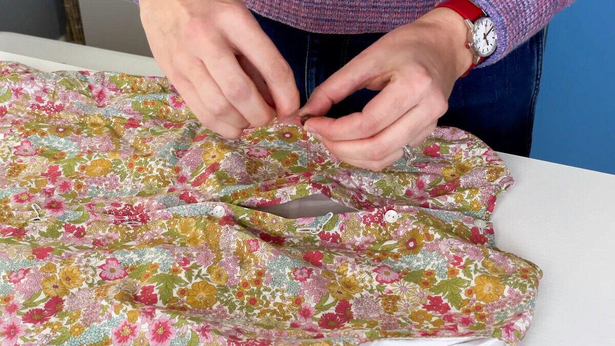 Close up of Erin Louis Fitzgerald hand sewing button onto floral dress