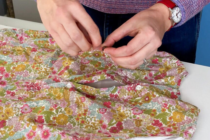 Close up of Erin Louis Fitzgerald hand sewing button onto floral dress