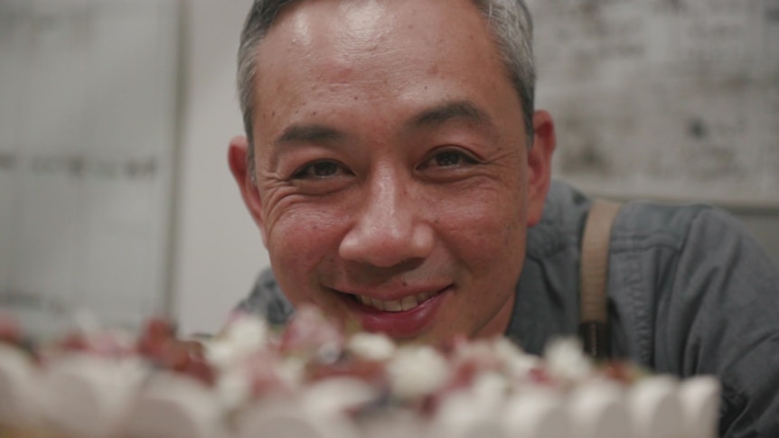 A close-up of a man staring at the camera with the frosting of cake seen in the foreground.